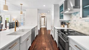 A modern kitchen with white cabinetry, a stainless steel stove, and a wooden floor.