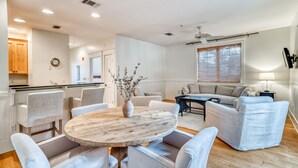 A modern living room with a round wooden table, grey sofas, and a kitchen area with wooden cabinets and a built-in oven. - Gracelyn Flat - Close to Shopping & Dining, Near Sky & Cabana Pool, Free Bikes/Fitness/Tennis (Rosemary Beach)