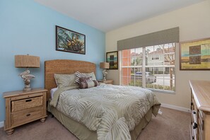 A bedroom with a bed, two nightstands, a window with blinds, and wall art. - Sunrise Crossing by VillaDirect (Kissimmee)