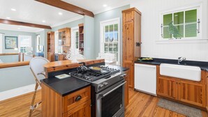 A modern kitchen with wooden cabinets, a black countertop, a built-in stove, and a window with green shutters. - Knoepp Cottage & Carriage House - Spectacular Gulf Views, South of 30A (Rosemary Beach)
