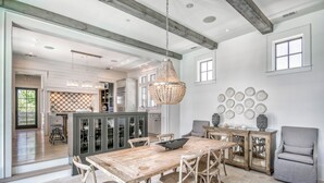 Un vaste espace dédié à la salle à manger, avec une table et des chaises en bois, un lustre et une vue sur la cuisine.