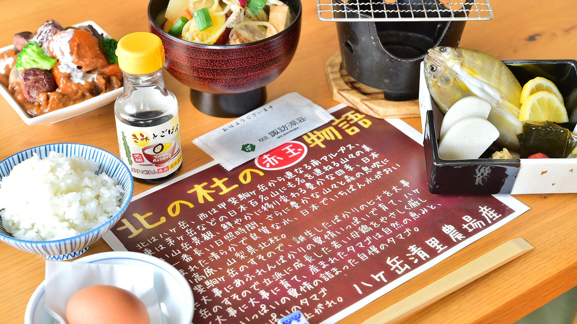 Pöydällä on erilaisia ruoka-aineita, kuten riisiä, lautanen keittoa, pullo kastiketta ja ruokalista, jossa on japaninkielistä tekstiä.