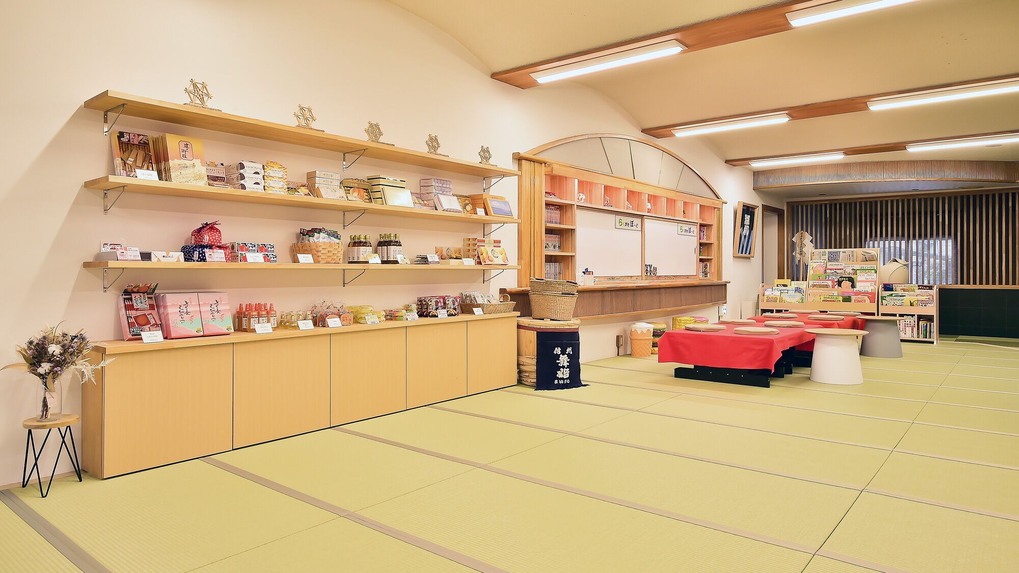 Una habitación japonesa tradicional con suelo de tatami, estantes de madera con diversos objetos y una mesa baja con mantel rojo.