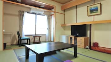 Una habitación tradicional japonesa con suelo de tatami, una mesita baja, una silla, un televisor y un mueble pequeño.