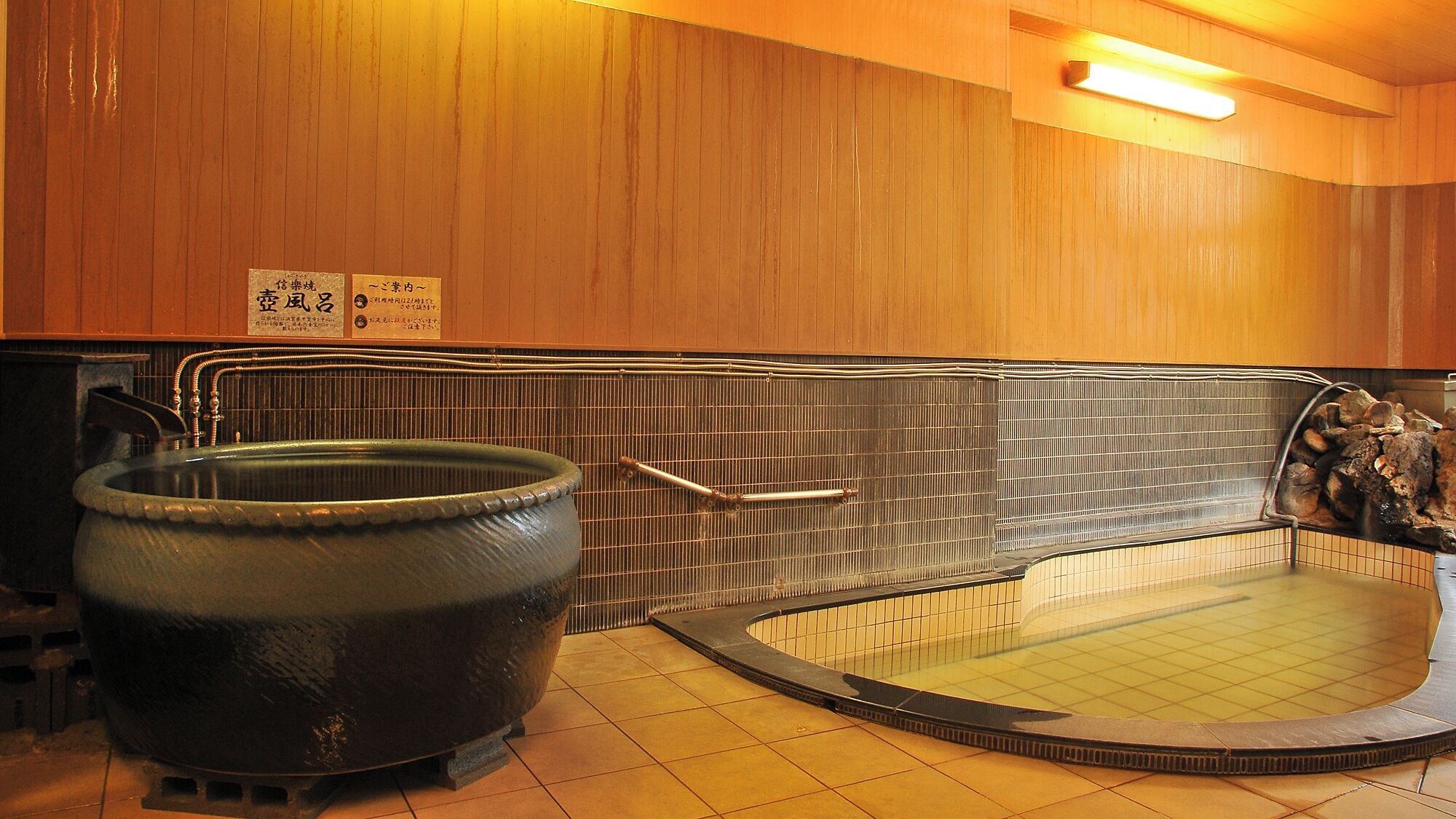 Un onsen japonés tradicional con una gran bañera de piedra caliente y un baño de piedra independiente.