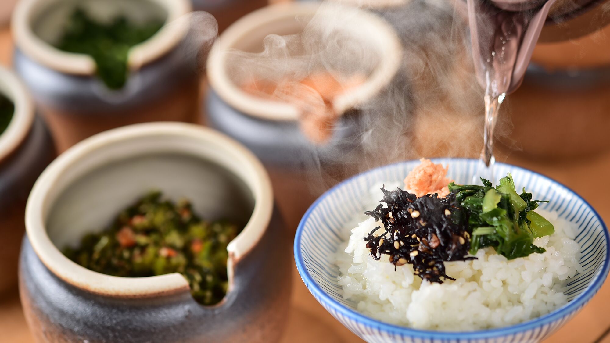 A bowl of rice topped with seaweed and vegetables, steam rising from the bowl.