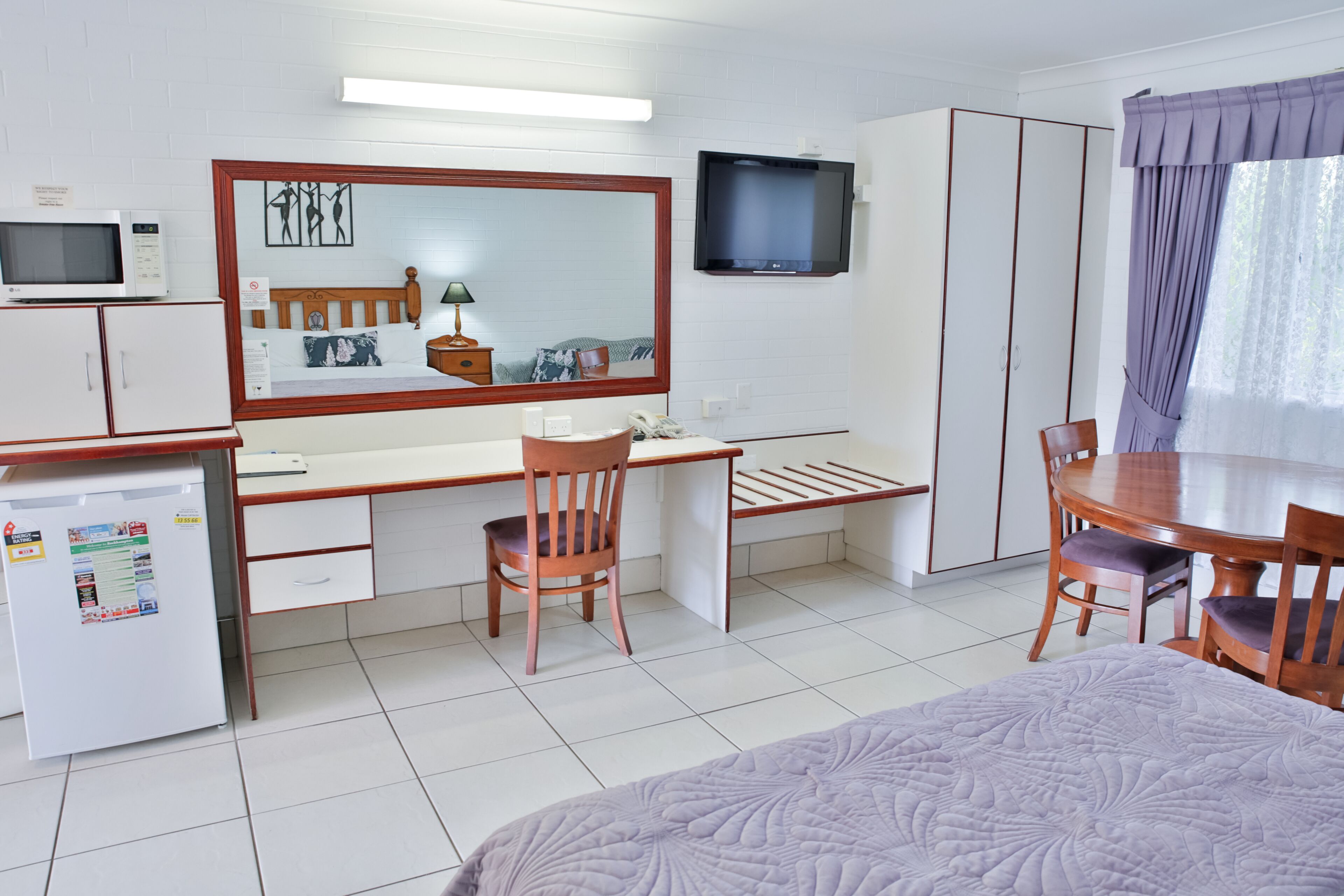 Una habitación de hotel con cama, escritorio con silla, televisor, armario y un refrigerador pequeño.
