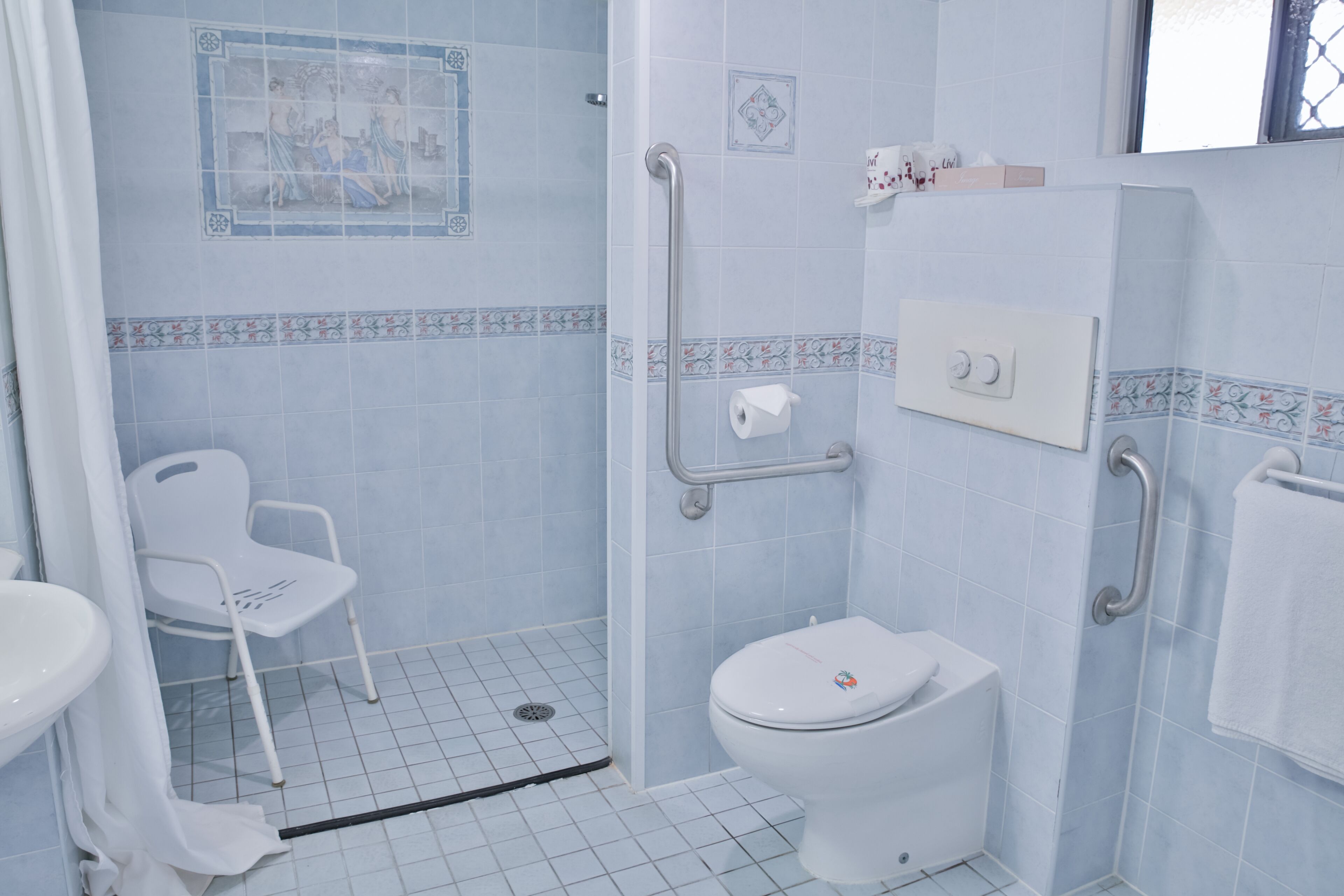 A bathroom with a shower, toilet, and a white chair.