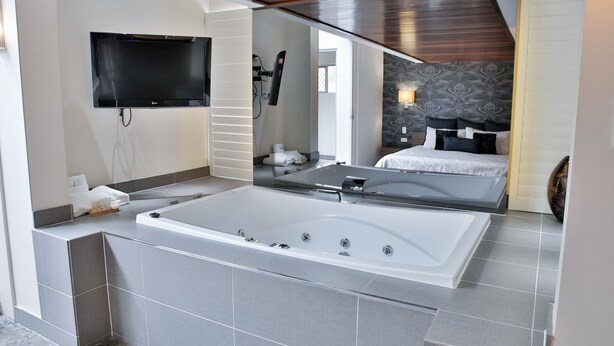 A modern bathroom with a large bathtub, a flat-screen TV mounted on the wall, and a separate shower area. - Central Park Motel (Allenstown)