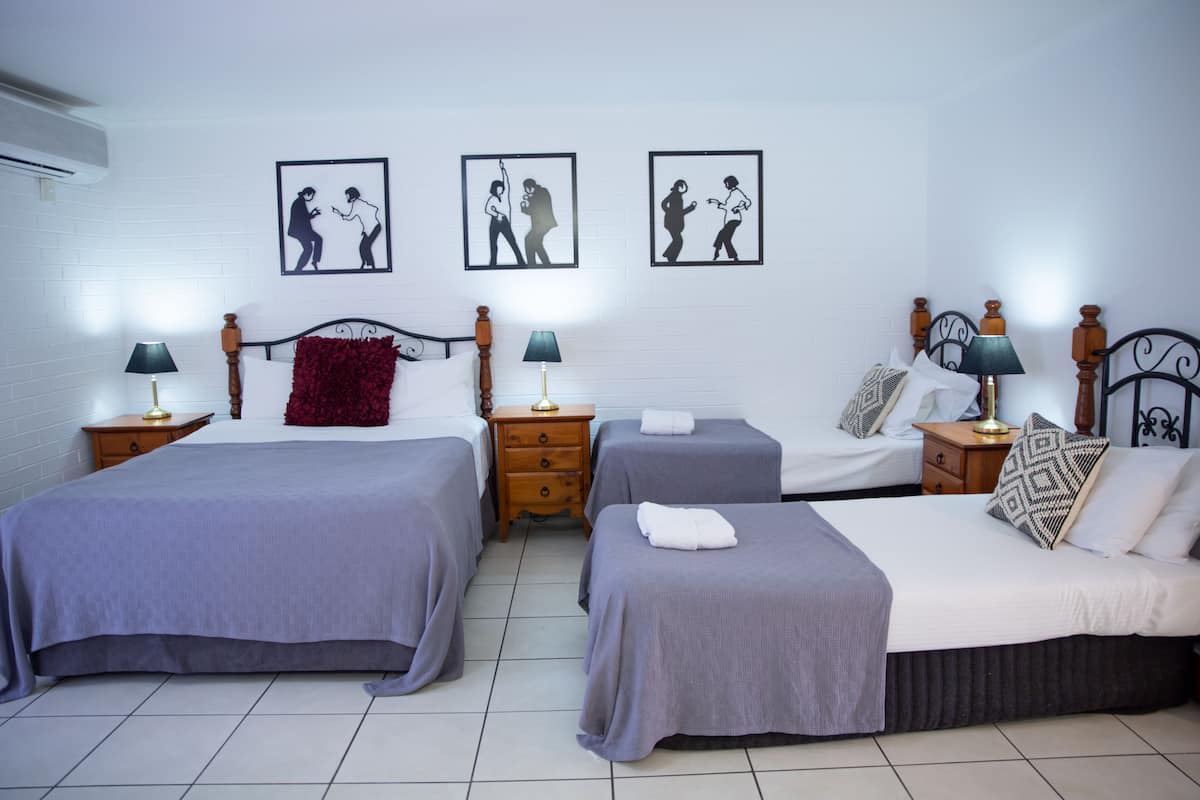A hotel room with two single beds, a double bed, and a nightstand with lamps. There are three framed pictures on the wall.