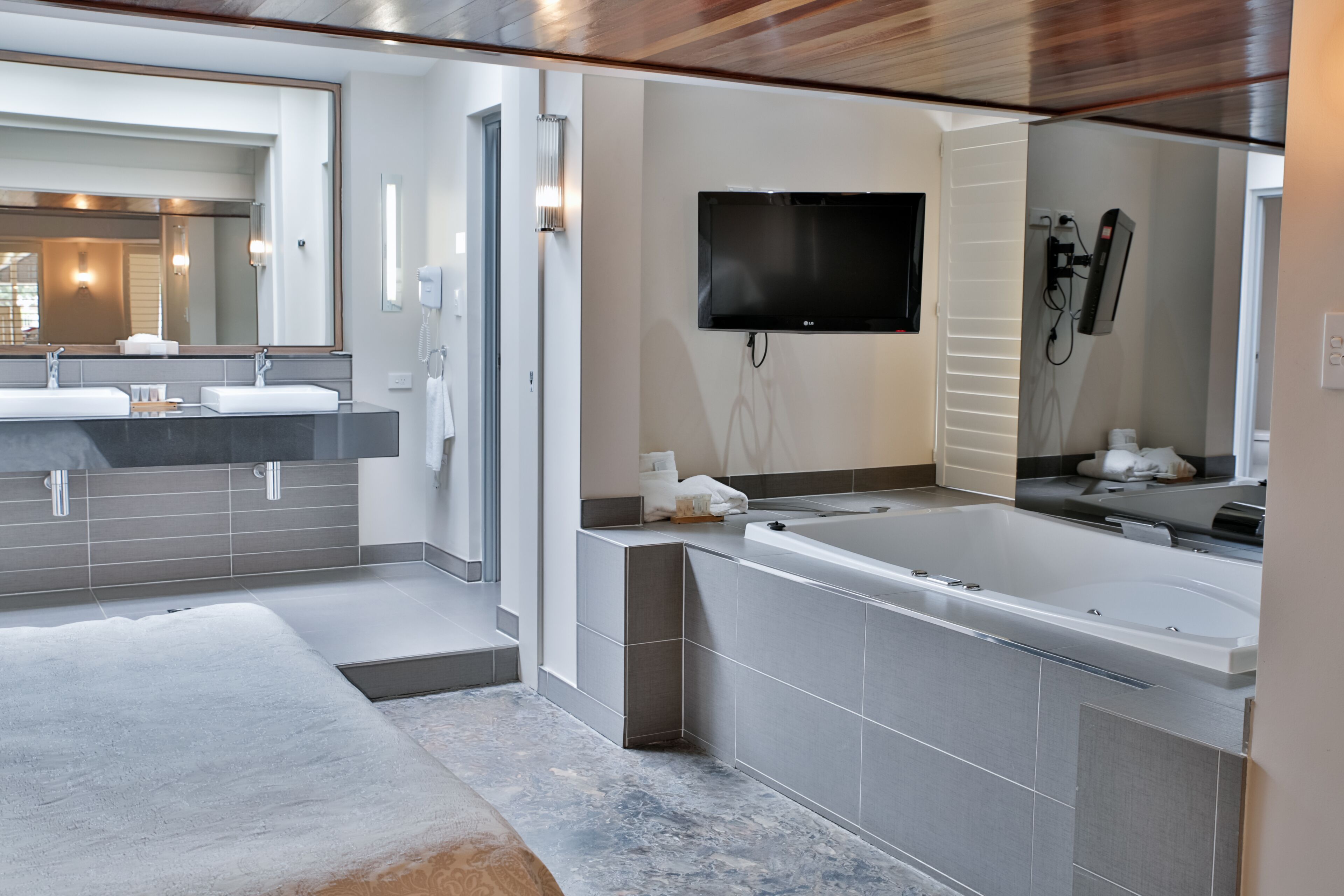 Un baño moderno con un espejo grande, dos lavamanos, una bañera y un televisor de pantalla plana.