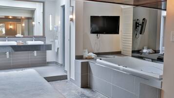 Un baño moderno con un espejo grande, dos lavamanos, una bañera y un televisor de pantalla plana.