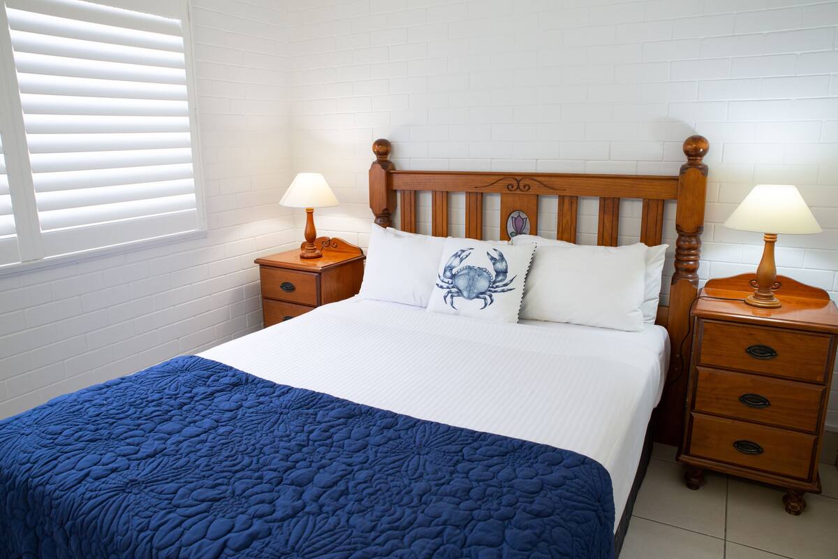 A neatly made bed with a blue quilt, two bedside tables with lamps, and a wooden headboard.