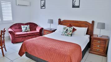 A bedroom with a large bed, a red sofa, two bedside tables with lamps, and a wooden nightstand.