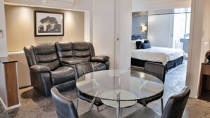 A modern hotel room with a leather sofa, a glass dining table, and a bed with a blue headboard. - Central Park Motel (Allenstown)