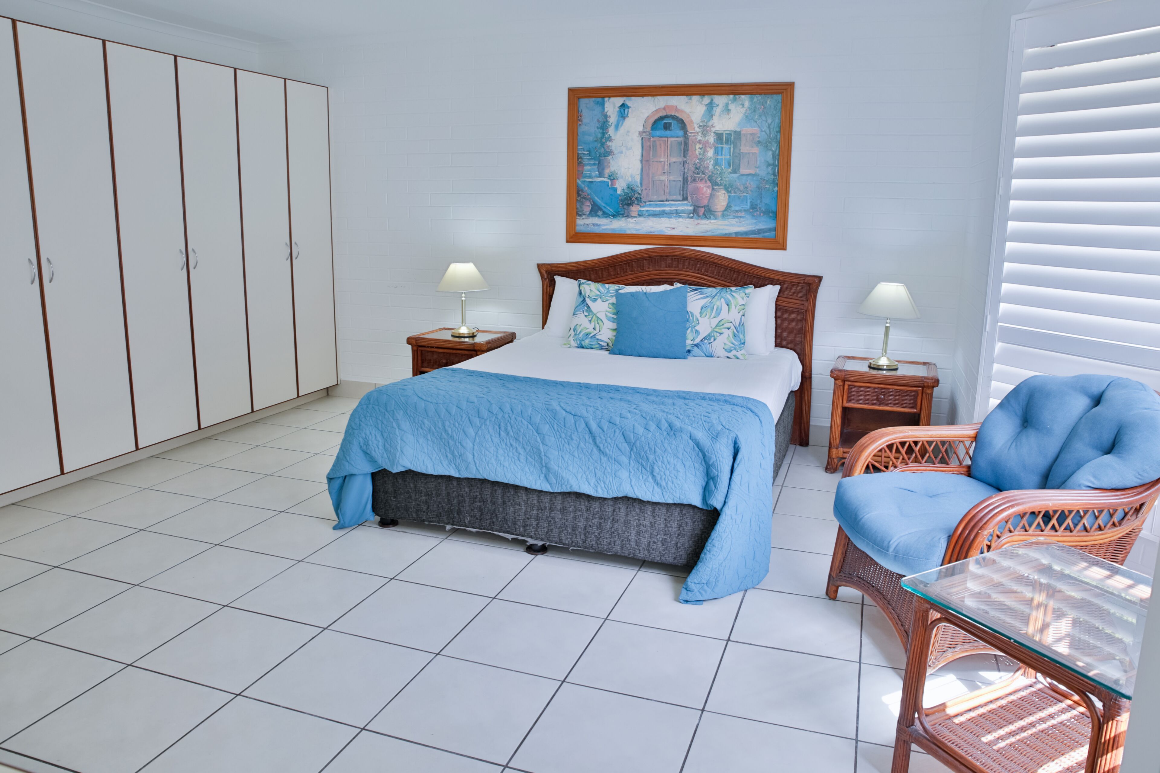 A bedroom with a bed, two nightstands, a chair, a wardrobe, and a painting on the wall.