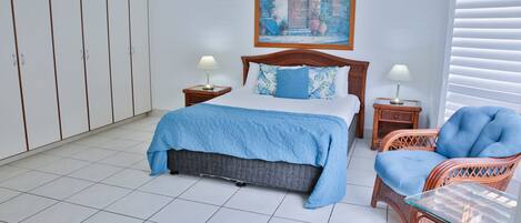 A bedroom with a bed, two nightstands, a chair, a wardrobe, and a painting on the wall.