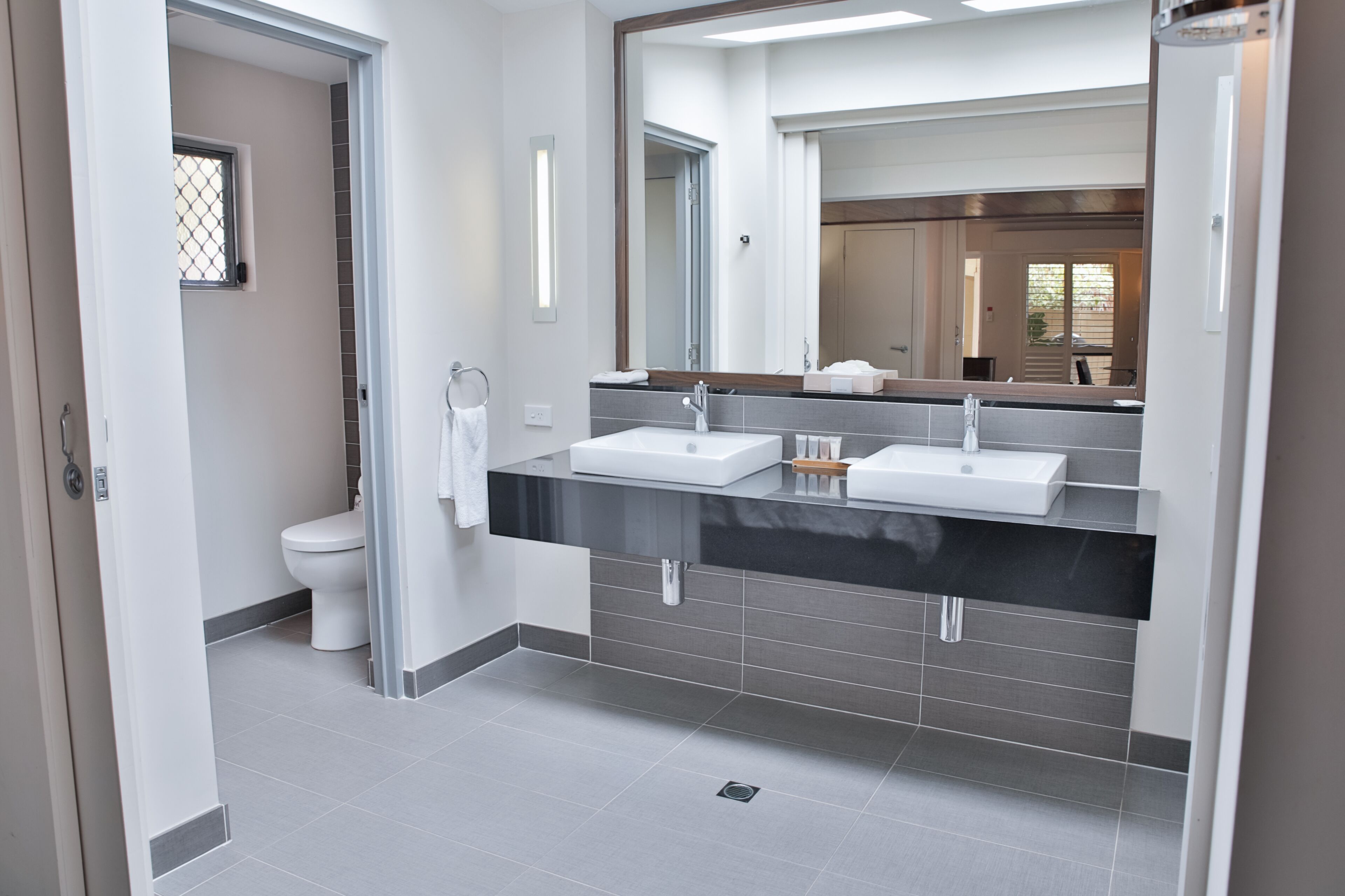 A modern bathroom with two sinks, a toilet, and a large mirror.