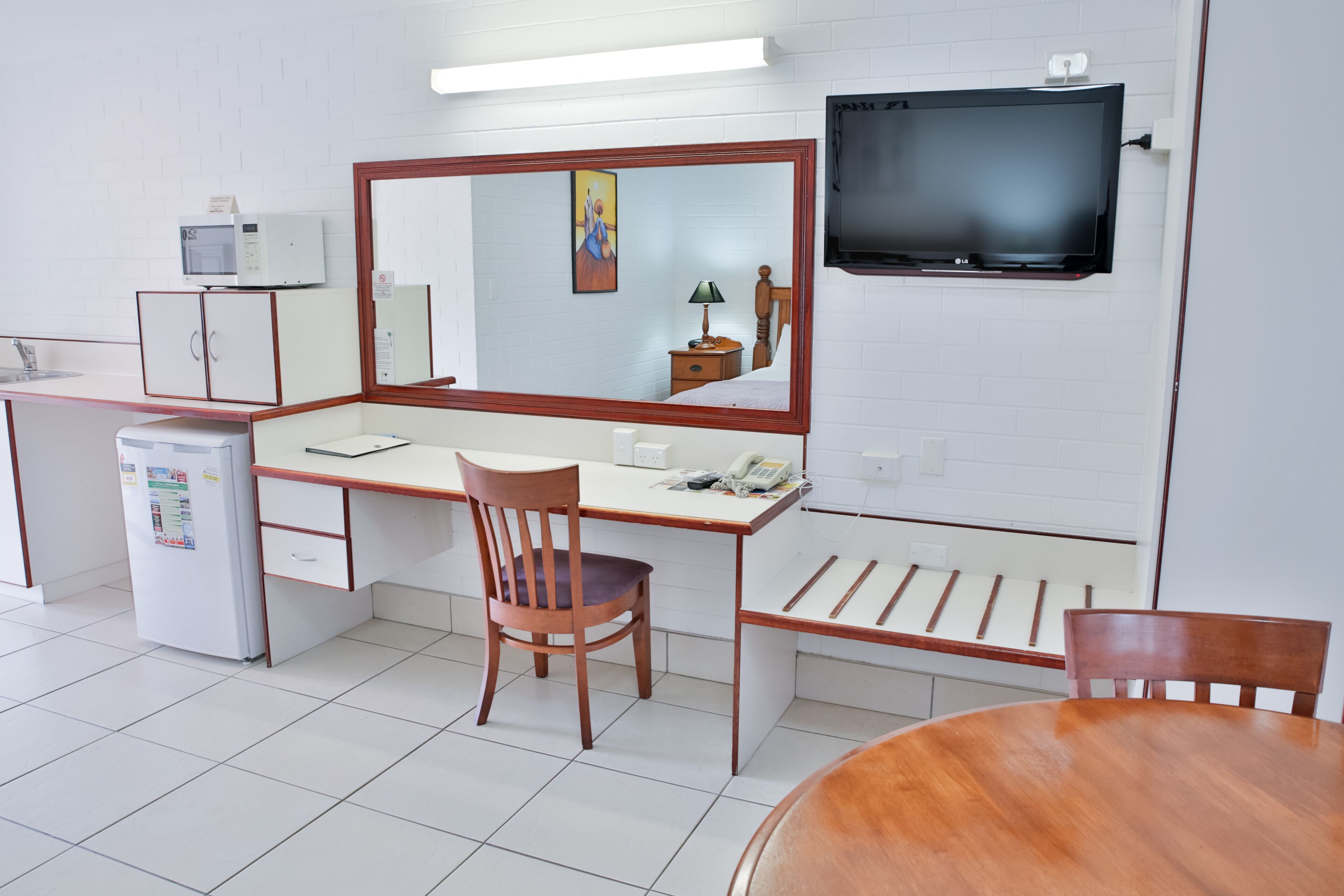 A hotel room with a desk, a chair, a bed, a television, a refrigerator, and a microwave.