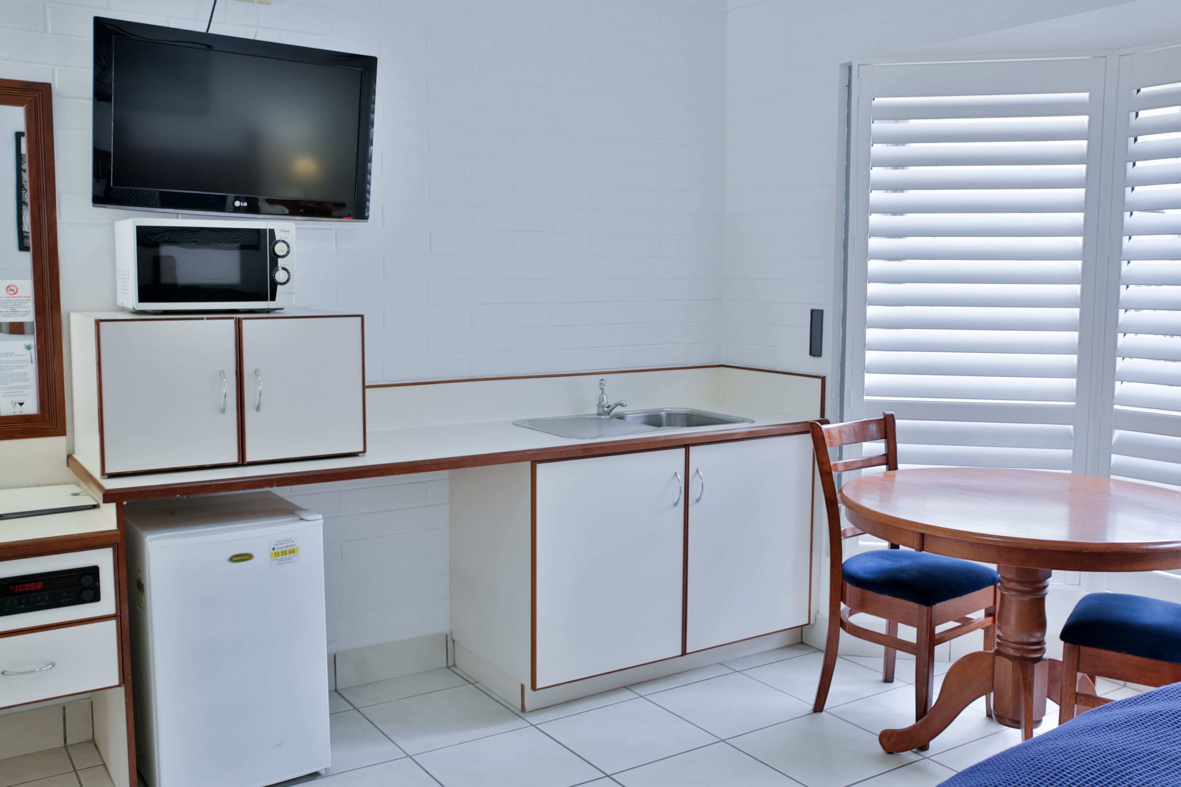 A compact kitchen with a microwave, refrigerator, and sink. There is a dining table with chairs and a television mounted above the counter.