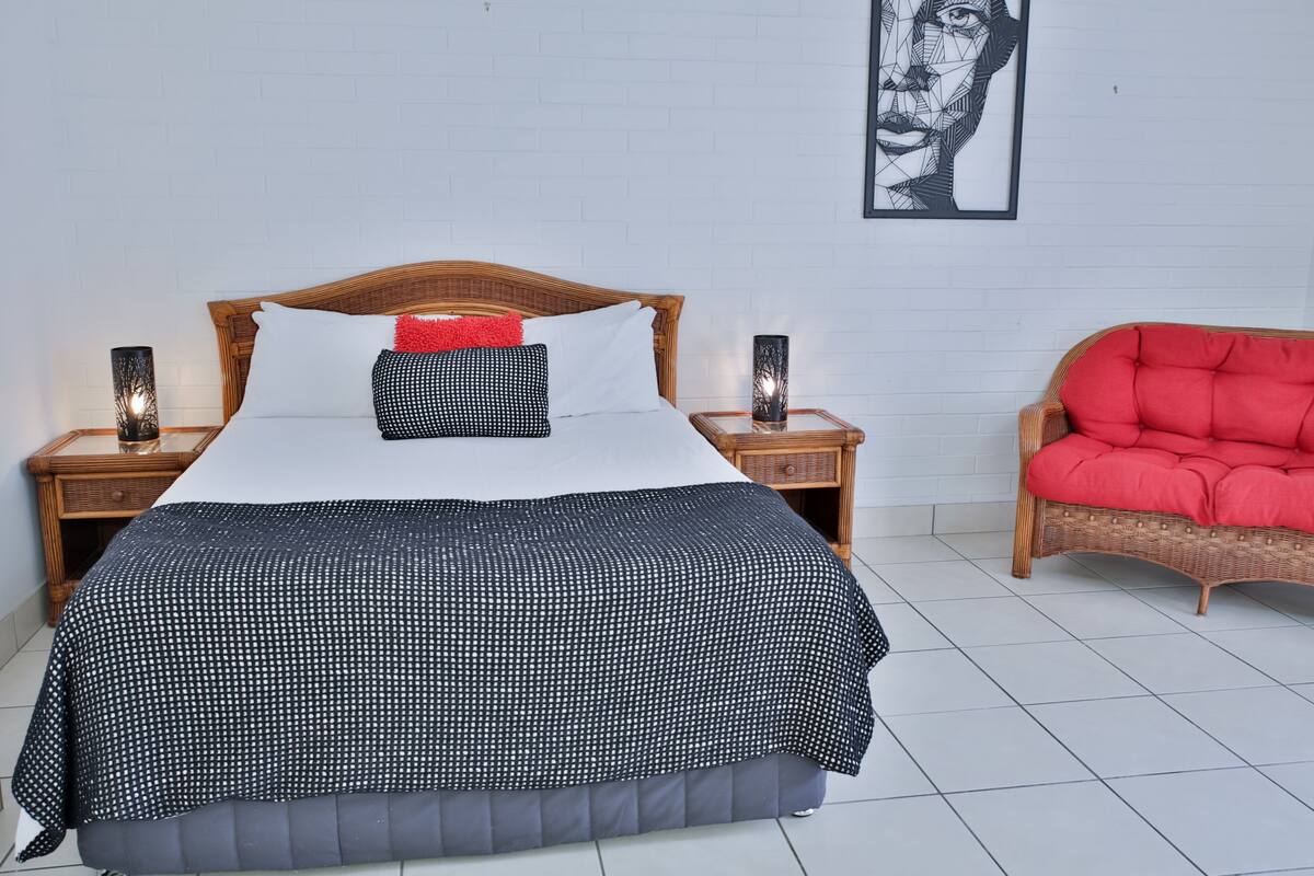 A neatly made bed with a polka dot bedspread, a red pillow, and two bedside lamps on wooden nightstands.