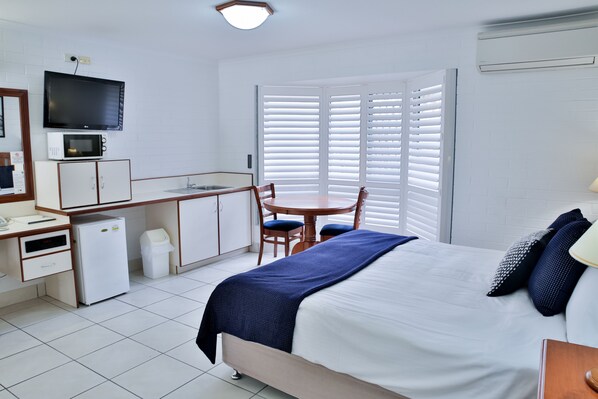 Habitación de hotel con una cama, un escritorio con computadora, microondas, refrigerador y televisión.