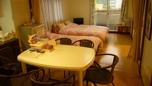 Et hotelværelse med spisebord, to senge, et køleskab, et lille tekøkken og en skydedør til balkonen.