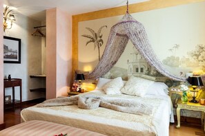 A bedroom with a canopy bed, a nightstand with a lamp, a wall-mounted shelf, and a framed picture.