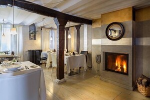 A dining area with a fireplace, wooden beams, and a view of the dining room.