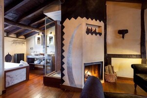 A rustic interior with a fireplace, wooden beams, a glass-enclosed bathroom, and a stone wall with a bull head decoration.