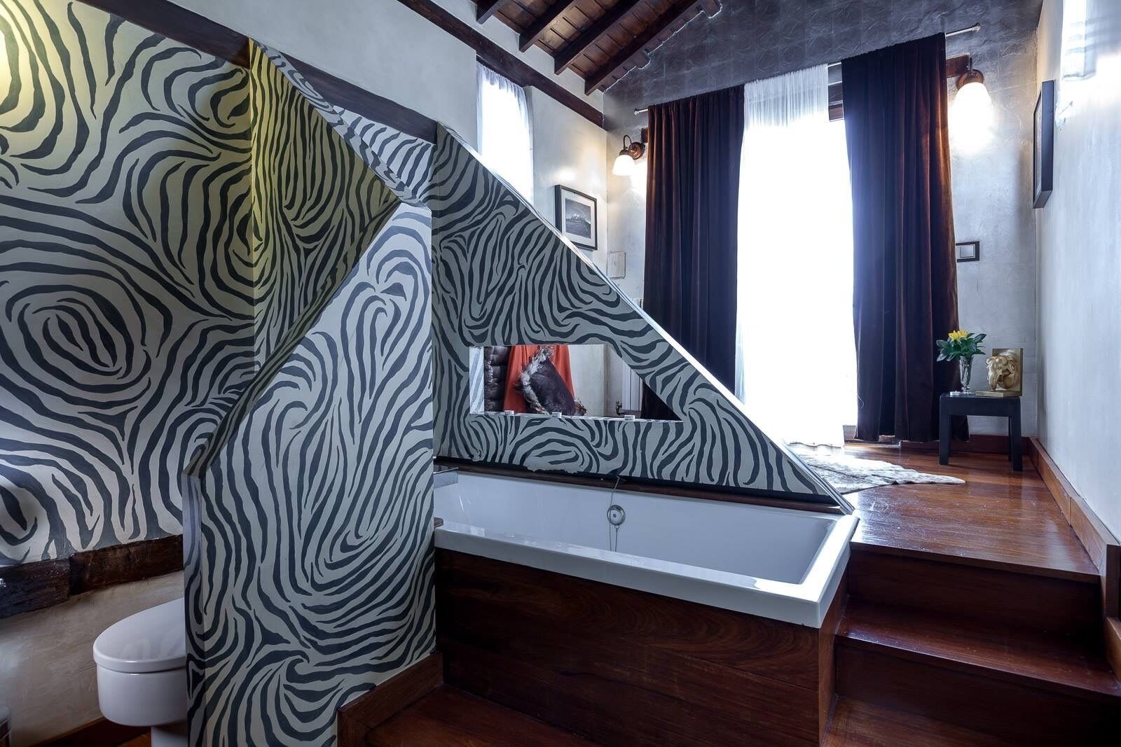 Een badkamer met een douchegordijn met zebraprint, een witte badkuip en houten vloeren.