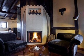 A cozy living room with a fireplace, two plush armchairs, a coffee table, and a rustic ceiling.