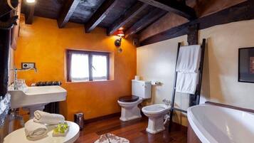 Un baño con vigas de madera, un lavamanos, dos inodoros, una bañera y un ventanal.