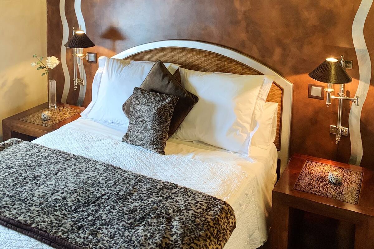 A bedroom with a bed, two bedside tables, a nightstand, a lamp, and a decorative wall.