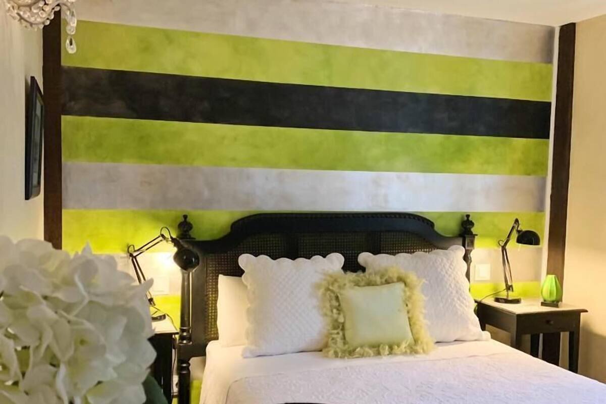 A bedroom with a bed, bedside tables, a chandelier, and a wall with horizontal stripes.