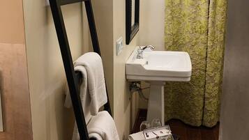 Un baño con lavabo blanco, un perchero con toalla, una mesita con artículos de aseo y una cortina de ducha verde con estampado.