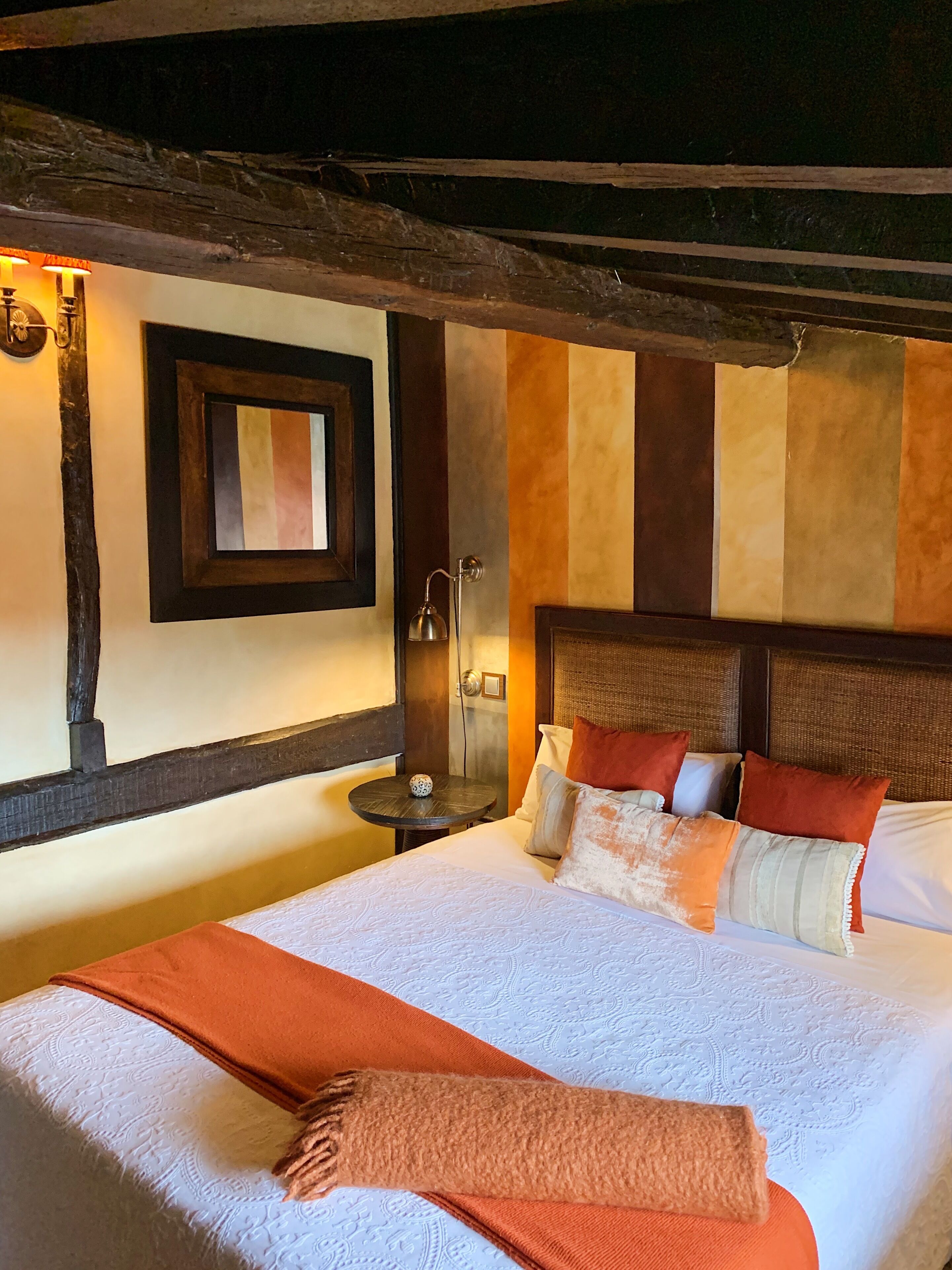 Ein Hotelzimmer mit einem großen Bett, einem kleinen runden Tisch, einem wandmontierten Spiegel und einer strukturierten Wand.
