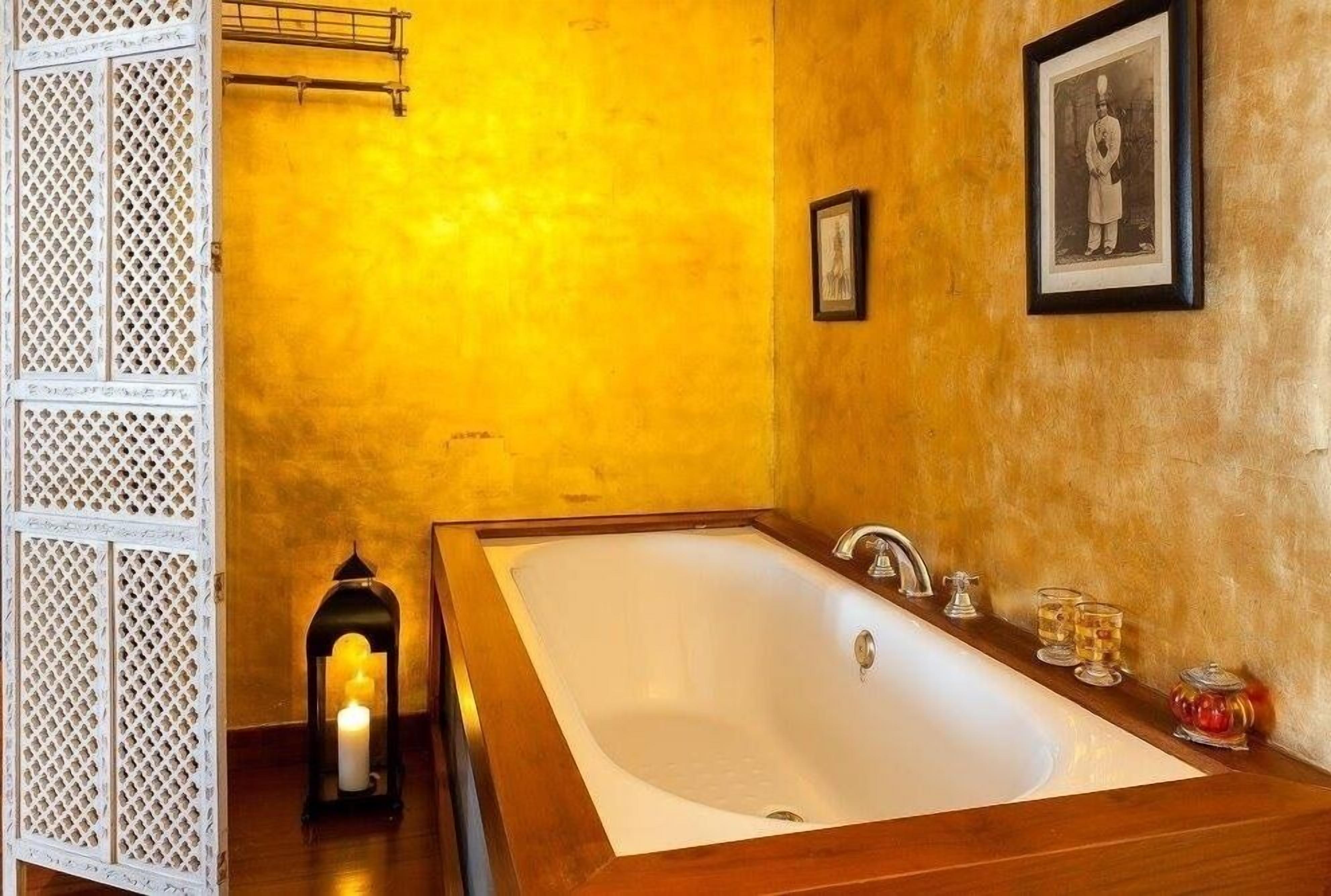 A bathroom with a large bathtub, a wooden vanity, a lit candle, and a framed picture on the wall.