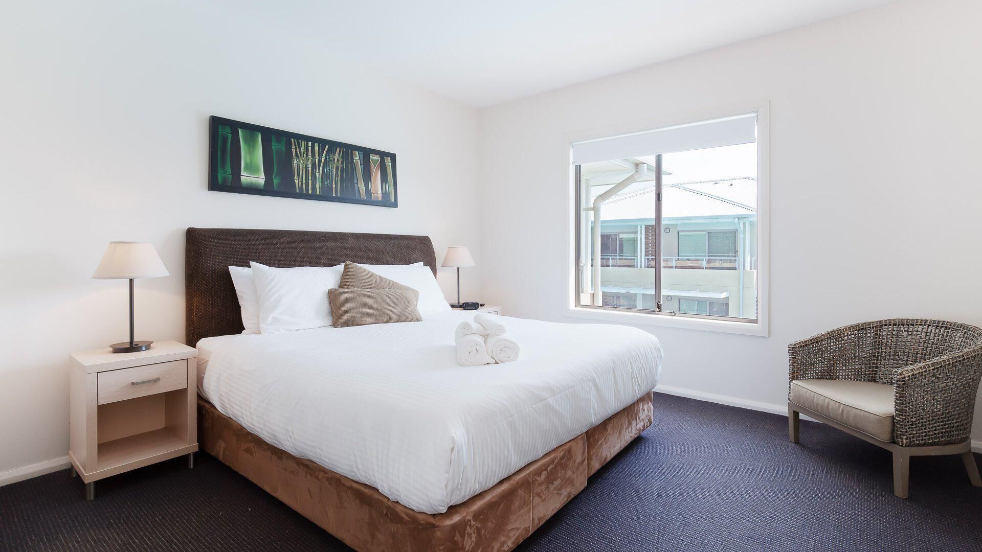 Une chambre d’hôtel avec un grand lit, deux tables de chevet, une chaise, une fenêtre donnant sur un beau paysage et un tableau au mur.