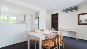 A modern kitchen with white cabinets, a built-in fridge, and a dining area with a white table set for four. - Pacific Blue  245-265 Sandy Point Rd - Dual Key Access, air conditioned unit with resort facilities and linen supplied (Salamander Bay)