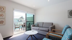 A modern living room with a grey sofa, a round coffee table, and a balcony with a pool view. - Pacific Blue  245-265 Sandy Point Rd - Dual Key Access, air conditioned unit with resort facilities and linen supplied (Salamander Bay)