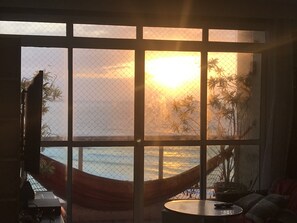 Une pièce dotée d’une grande fenêtre donnant sur une plage au coucher du soleil.