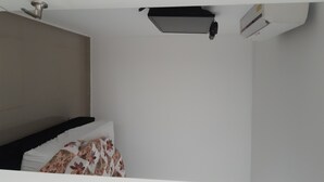 Ein Schlafzimmer mit einem Bett, einem Kopfkissen, einer Deckenleuchte und einer Wand-Klimaanlage.