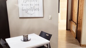 A dining area with a white table and black chairs, a decorative sign on the wall, and a hallway leading to another room.