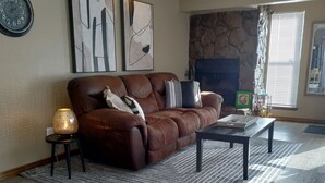A living room with a brown leather sofa, a coffee table, a rug, a fireplace, and artwork on the wall.