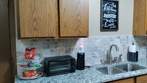 A kitchen with wooden cabinets, a granite countertop, a toaster, a coffee maker, a sink, and a microwave.