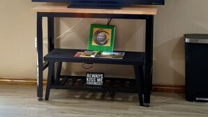A television on a wooden stand with a wall-mounted shelf above it.