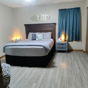 Un dormitorio con cama, mesitas de noche, una lámpara de pared y una ventana con cortinas.