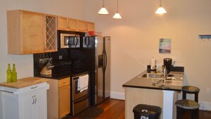 Cocina compacta con armarios de madera, estufa negra, refrigerador de acero inoxidable y una pequeña isla con pileta.