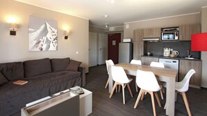 A modern living room with a sofa, dining table, and chairs. There is a kitchen area with a microwave and a refrigerator. - Studio avec Wi-Fi Gratuit + Accès Piscine! (Pra Loup)